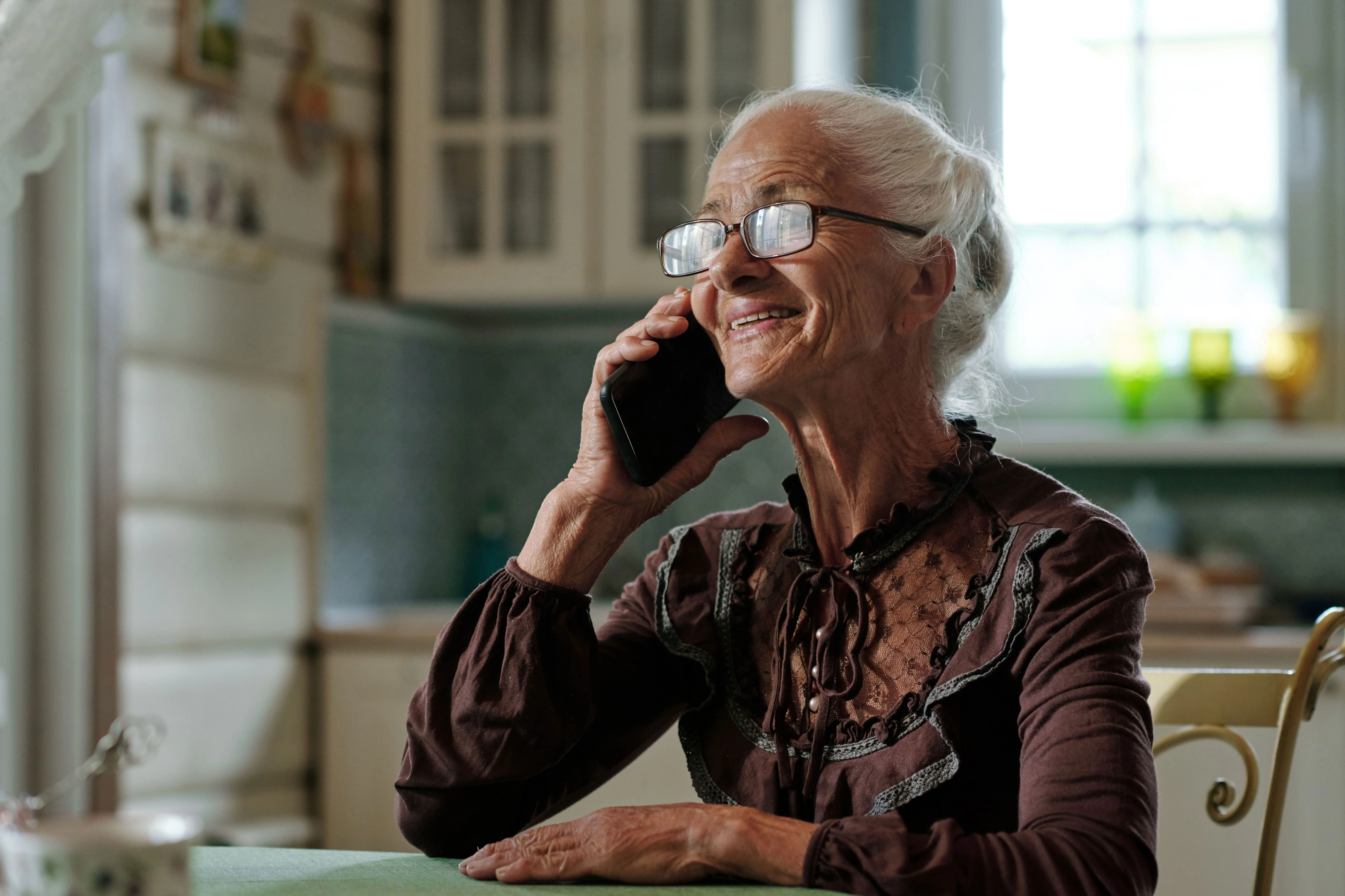 Äldre kvinna som ler under ett telefonsamtal i sitt kök